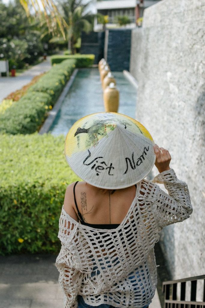 Back view of a woman wearing a Vietnamese hat walking down a garden path.