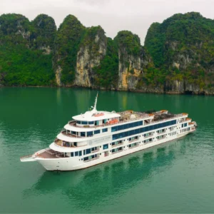 Ambassador Cruise luxury day tour ship cruising through emerald green waters past towering Halong Bay karsts.
