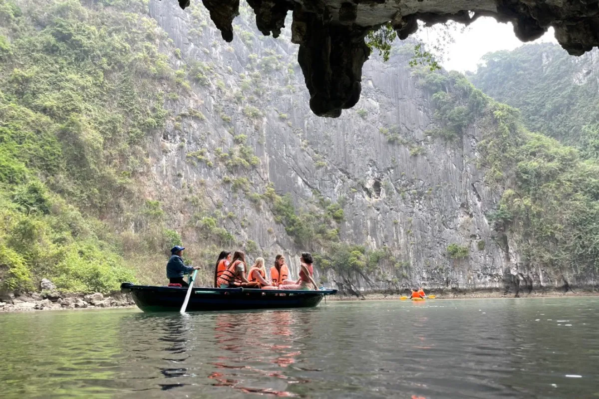 Passengers on a traditional bamboo rowboat passing under a low limestone cave arch in Halong Bay