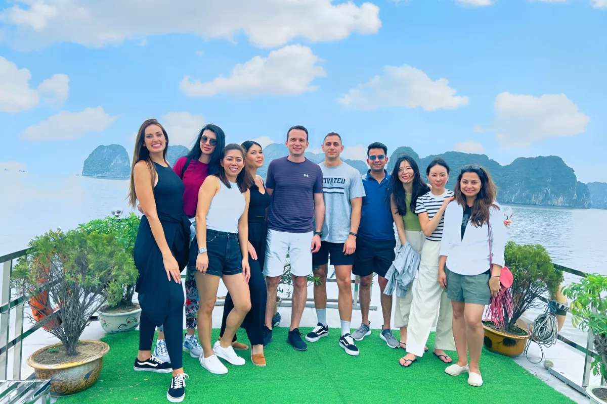 Group of international travelers posing on a cruise boat deck with Halong Bay limestone karsts in the background