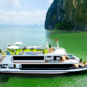 Liberty Cruise boat with rooftop deck sailing between limestone cliffs on Halong Bay day tour