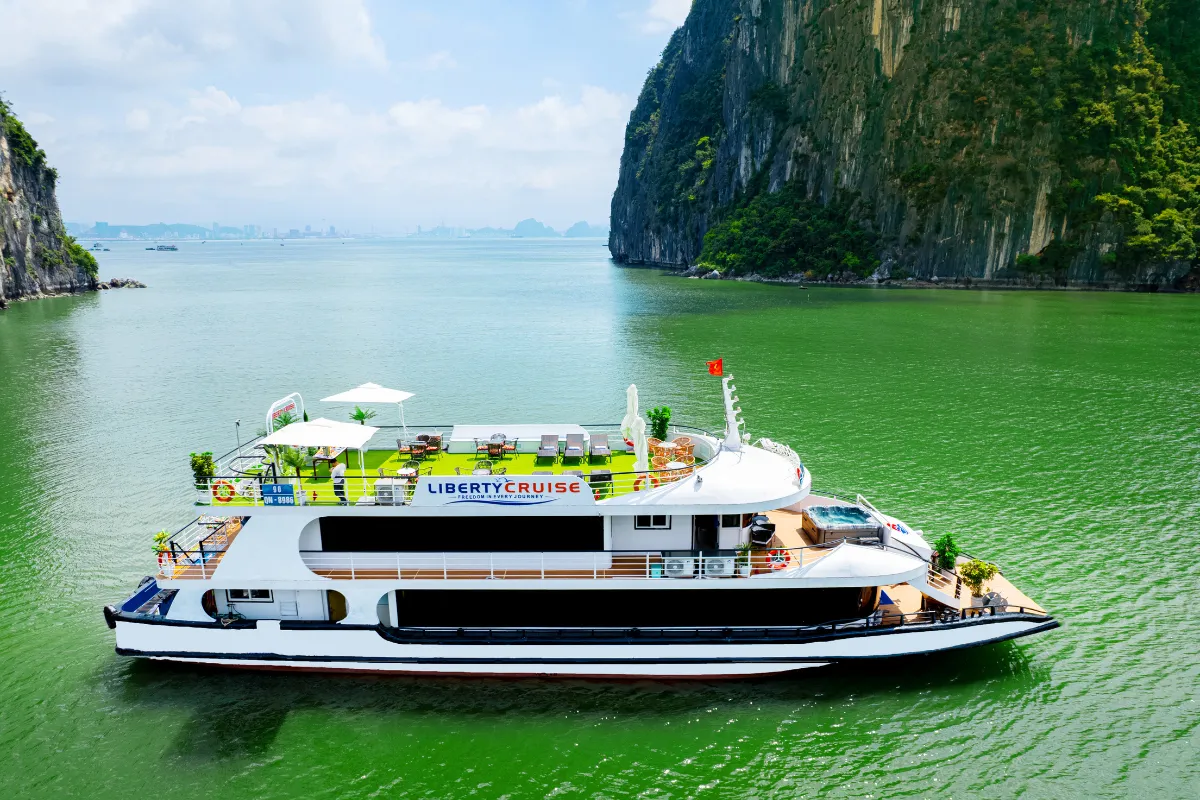 Liberty Cruise boat with rooftop deck sailing between limestone cliffs on Halong Bay day tour