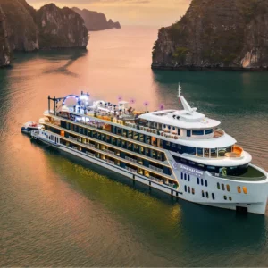 Luna Halong Cruise ship illuminated at sunset sailing through Halong Bay limestone islands