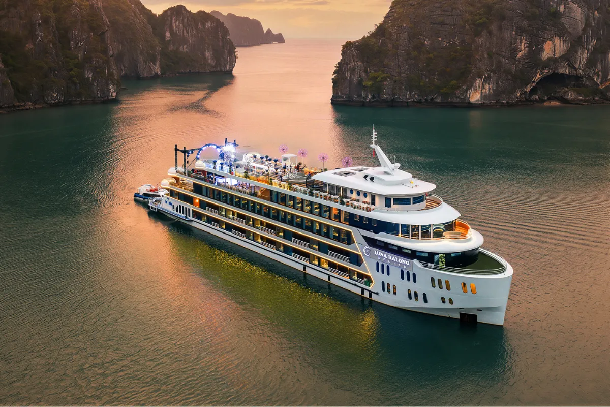 Luna Halong Cruise ship illuminated at sunset sailing through Halong Bay limestone islands
