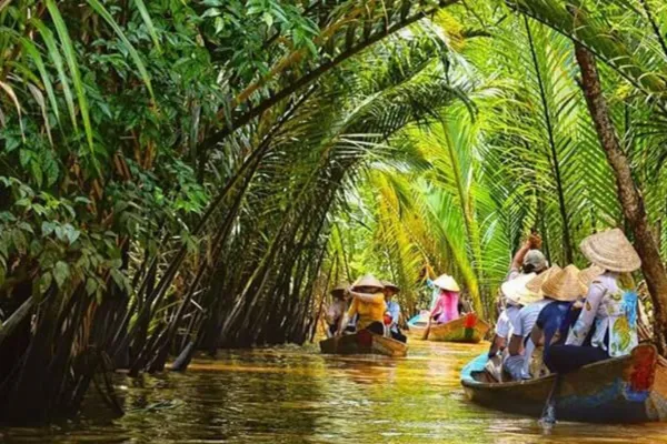 Tourists riding small boats through a narrow coconut-palm-lined canal in the Mekong Delta