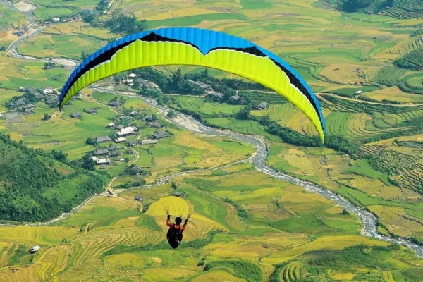 A paraglider flying over golden terraced rice fields and a river valley in Mu Cang Chai