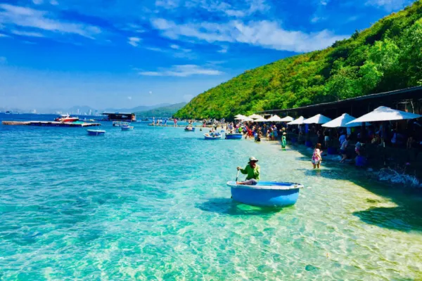 Tourists relaxing on a clear turquoise beach with small boats near a green island in Nha Trang Bay