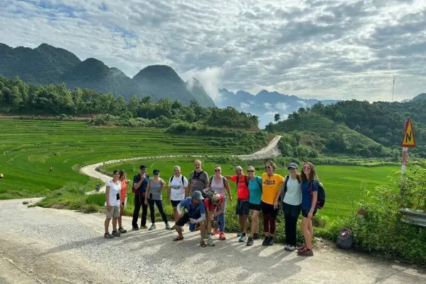 A group of trekkers posing at a scenic viewpoint overlooking rice terraces and karst mountains in Pu Luong
