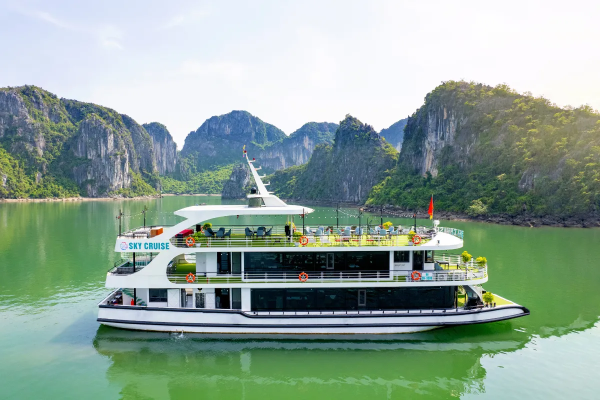 Sky Cruise boat anchored on calm green water surrounded by Halong Bay limestone mountains
