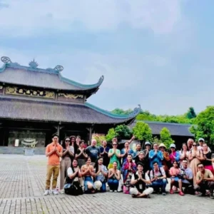 A large Bai Dinh Pagoda tour group posing in prayer gesture before Bai Dinh Pagoda's temple and tower