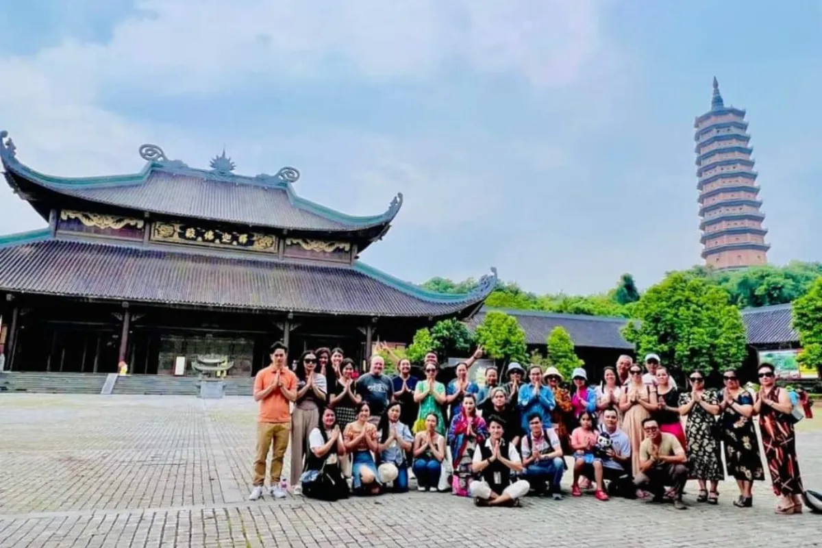 A large Bai Dinh Pagoda tour group posing in prayer gesture before Bai Dinh Pagoda's temple and tower