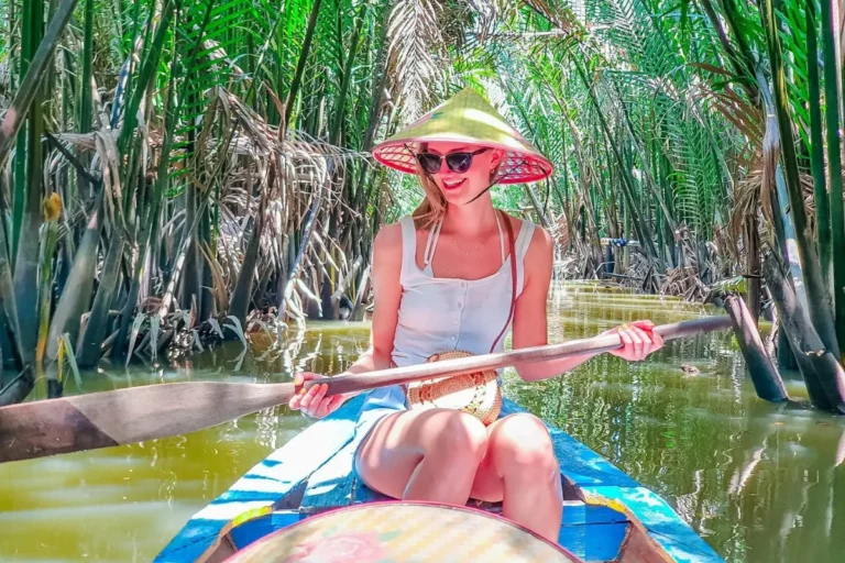 About Us 14 Woman paddling a small boat through a narrow coconut palm-lined canal in Ben Tre, Mekong Delta