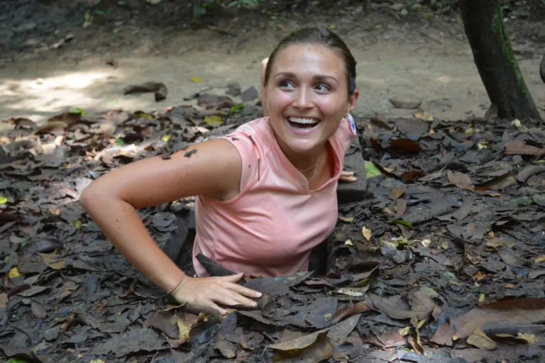 About Us 15 Smiling visitor climbing out of a narrow underground opening at the Cu Chi Tunnels near Ho Chi Minh City