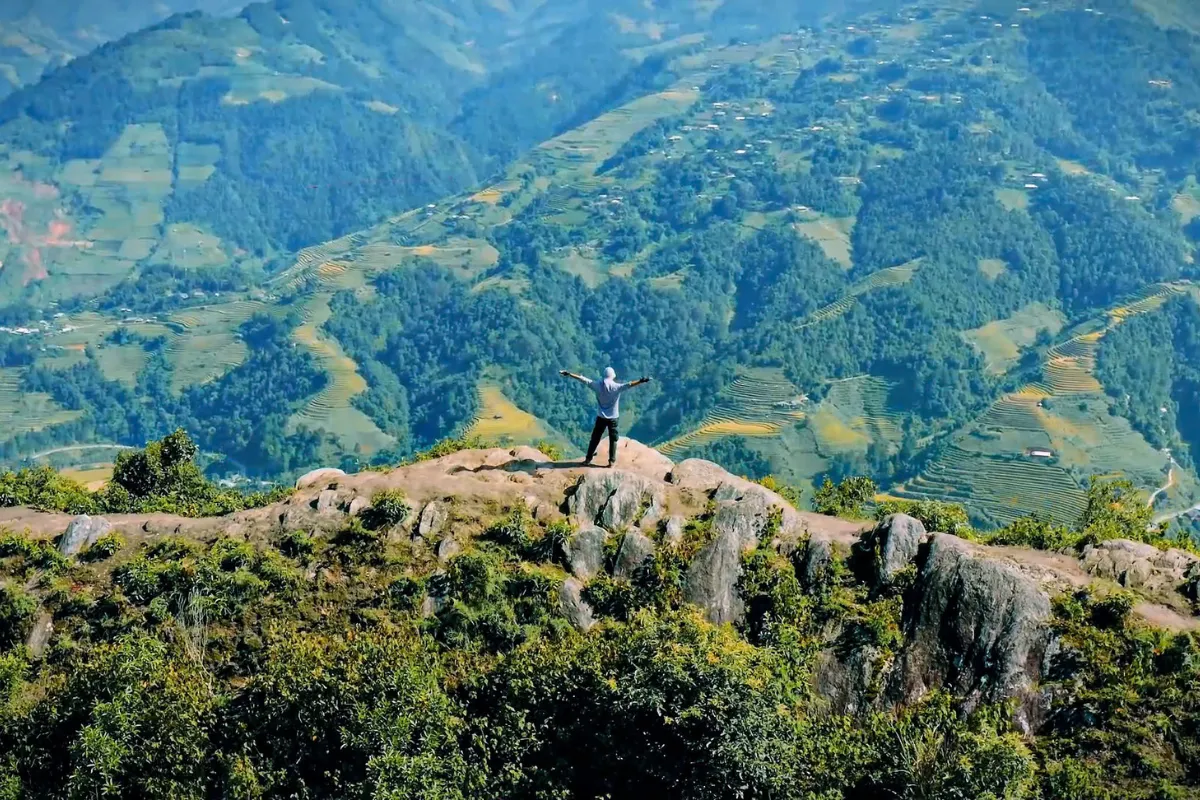 A hiker standing with arms outstretched on the narrow Dinosaur's Spine ridge overlooking Mu Cang Chai's terraced valley
