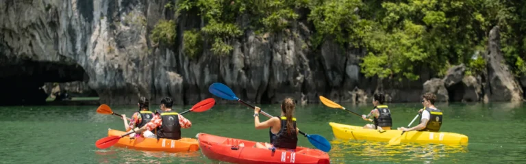 Tourists kayaking in colorful kayaks near a limestone cave entrance in Halong Bay