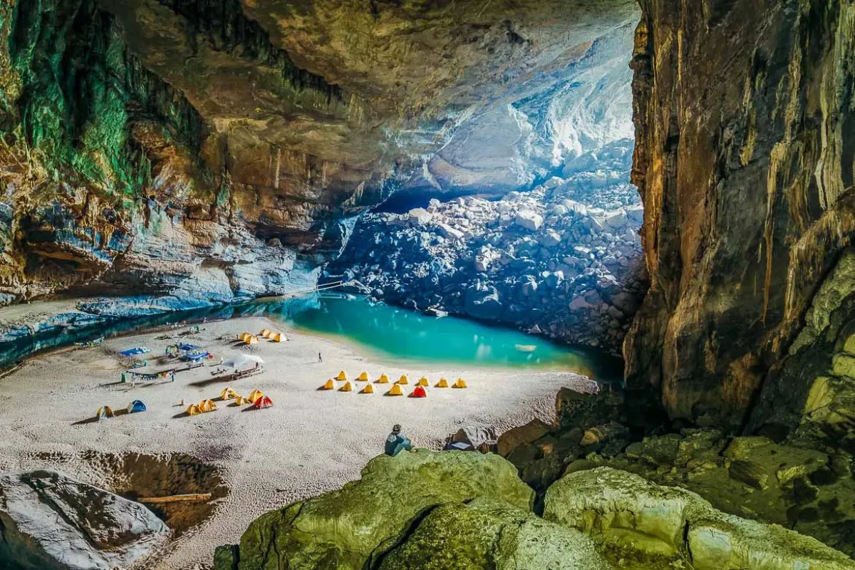 Camping tents on a sandy beach beside a turquoise lake inside the massive Hang En Cave, Phong Nha