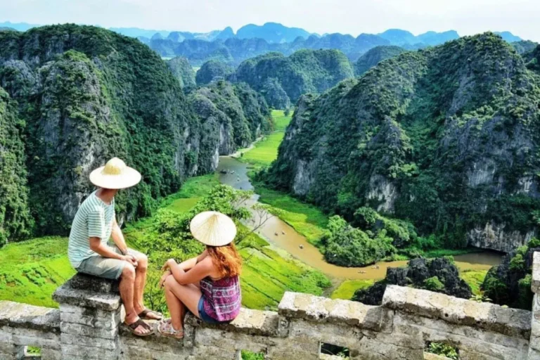 About Us 10 Two travelers in conical hats admiring the karst valley and winding river from Hang Mua viewpoint near Trang An
