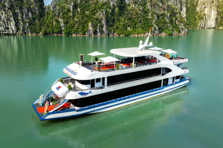 Aerial view of Harmony cruise ship gliding past towering limestone karsts on the Harmony Halong Bay day cruise tour