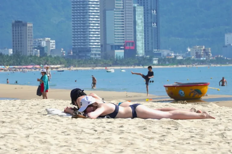 About Us 12 Sunbathers relaxing on My Khe Beach with Da Nang's high-rise skyline in the background