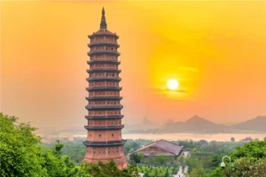 The Bao Thien Stupa of Bai Dinh Pagoda silhouetted against an orange sunset sky in Ninh Binh