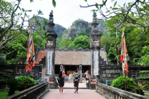 Visitors walking through the ornate stone gateway of King Dinh Temple with karst mountains behind, Ninh Binh