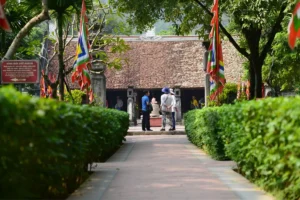 Tourists walking along a tree-lined stone path toward the tiled-roof Le Temple in Ninh Binh Province