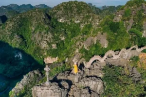 Woman in a yellow dress standing on the dragon-spine rock ridge at Ngoa Long Peak above Ninh Binh's karst valley