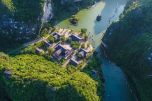 Aerial view of Vu Lam Ancient Palace nestled among limestone cliffs with boats navigating the surrounding river, Ninh Binh