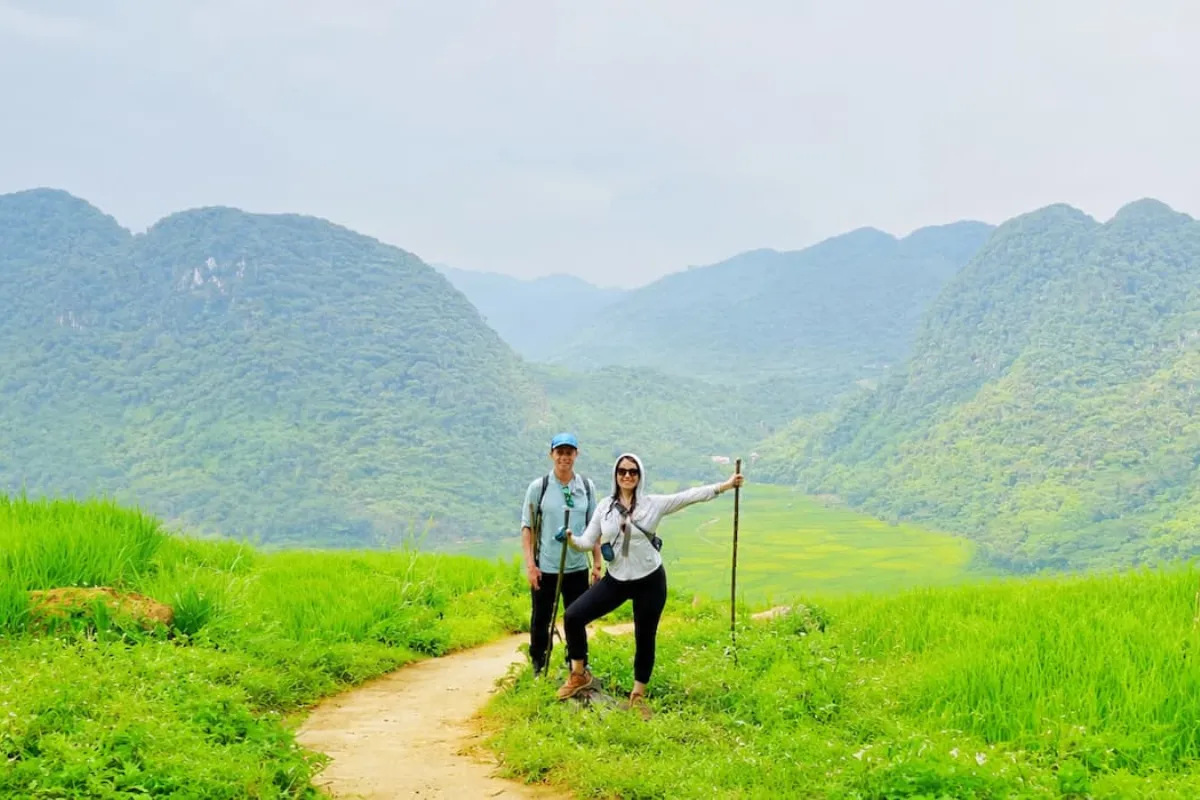 Two hikers with trekking poles overlooking a mountain valley and rice fields from a Pu Luong peak trail