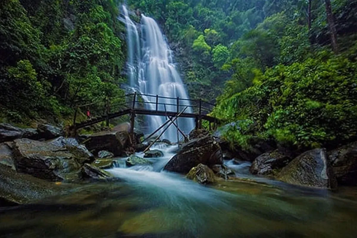 A multi-tiered waterfall cascading over rocks in a forested area near Mu Cang Chai