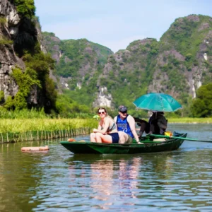 Tourists riding a sampan boat past limestone karsts on the Tam Coc day tour river route