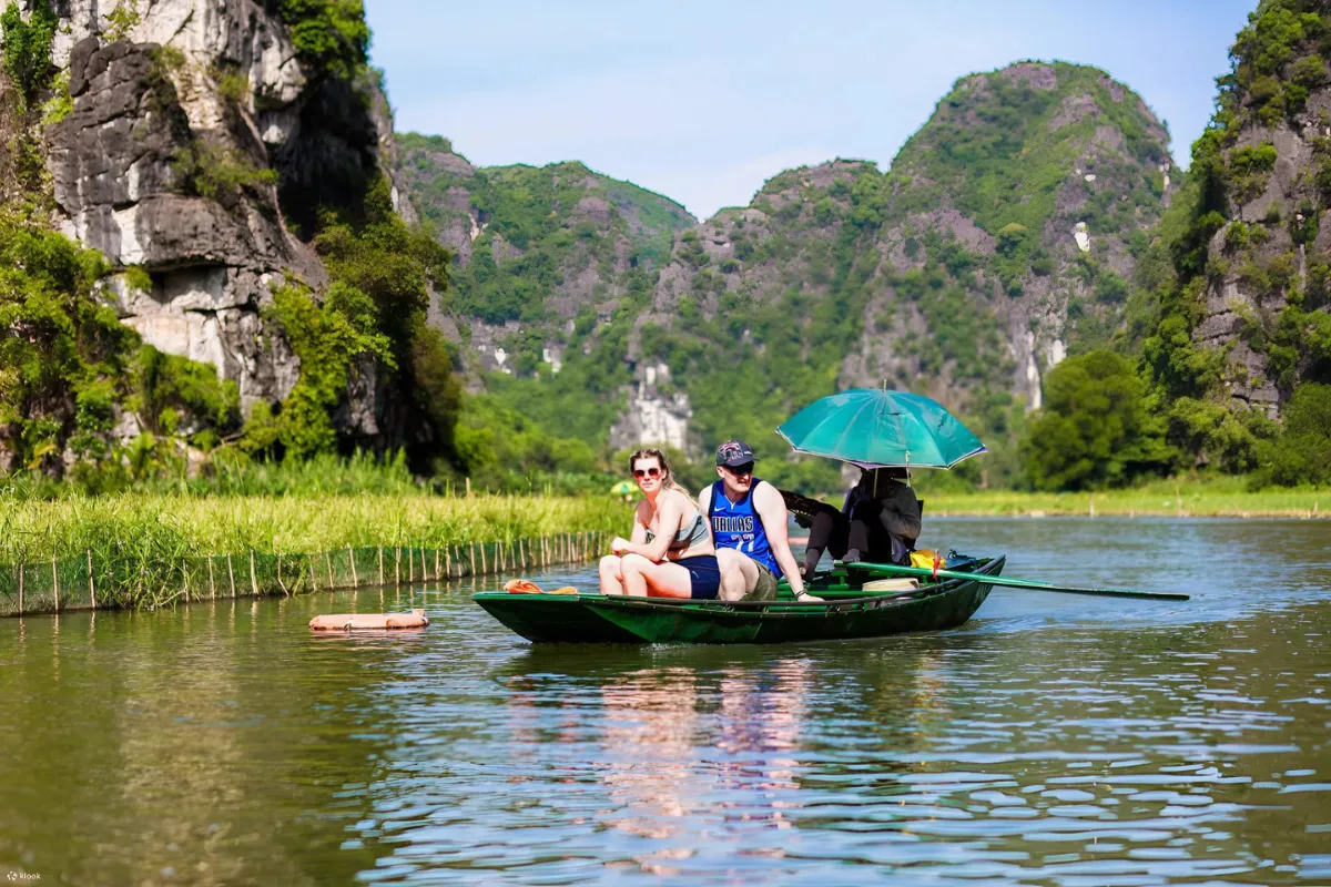 Tourists riding a sampan boat past limestone karsts on the Tam Coc day tour river route