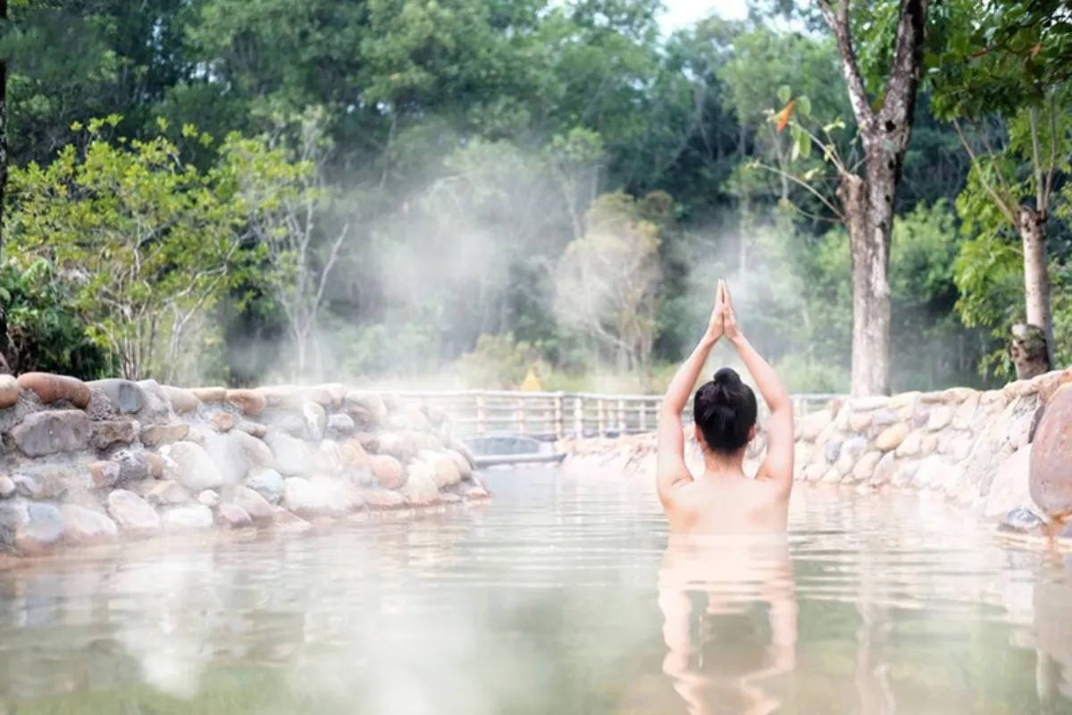 A woman relaxing in a steaming natural hot spring pool surrounded by forest near Tram Tau, close to Mu Cang Chai