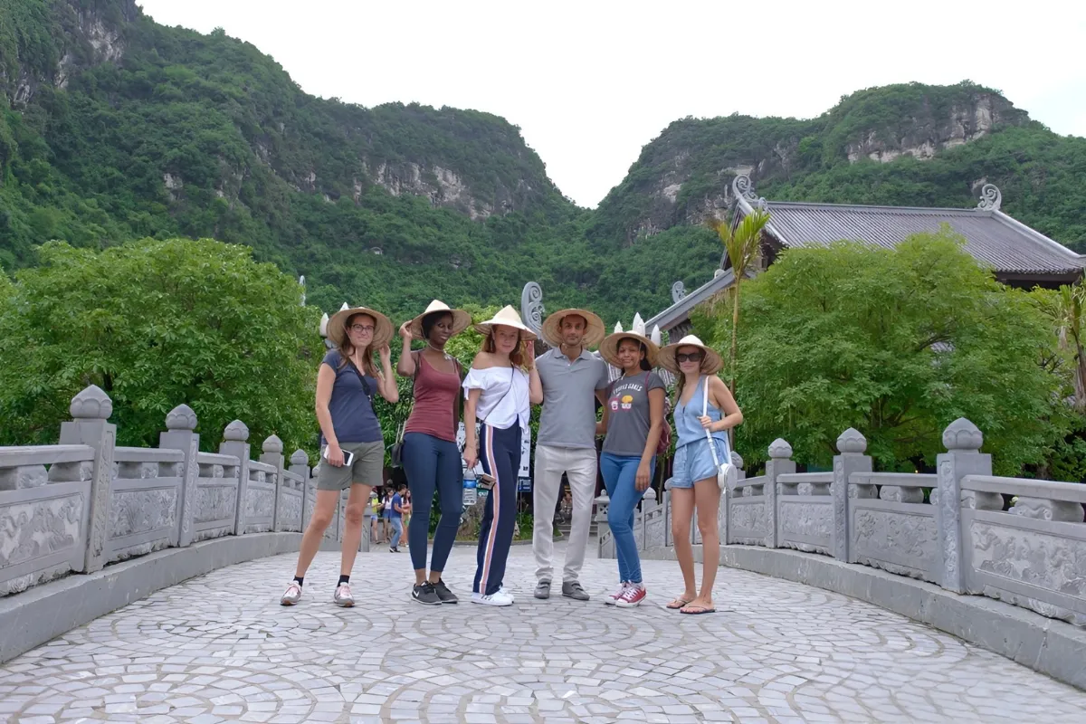 Tour group wearing conical hats on a stone bridge on Trang An Bai Dinh Pagoda Tour