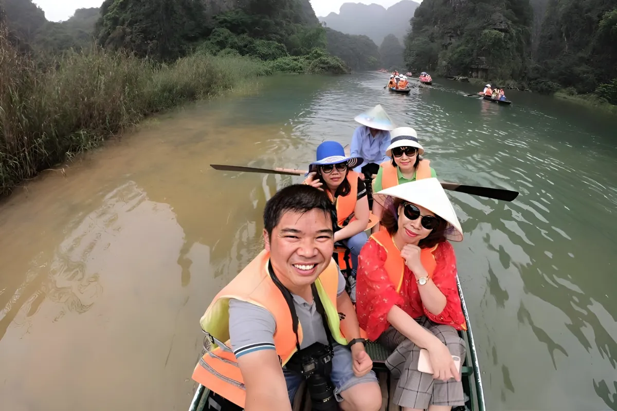 Tourists in life jackets take a boat selfie on the Trang An Hoa Lu tour river