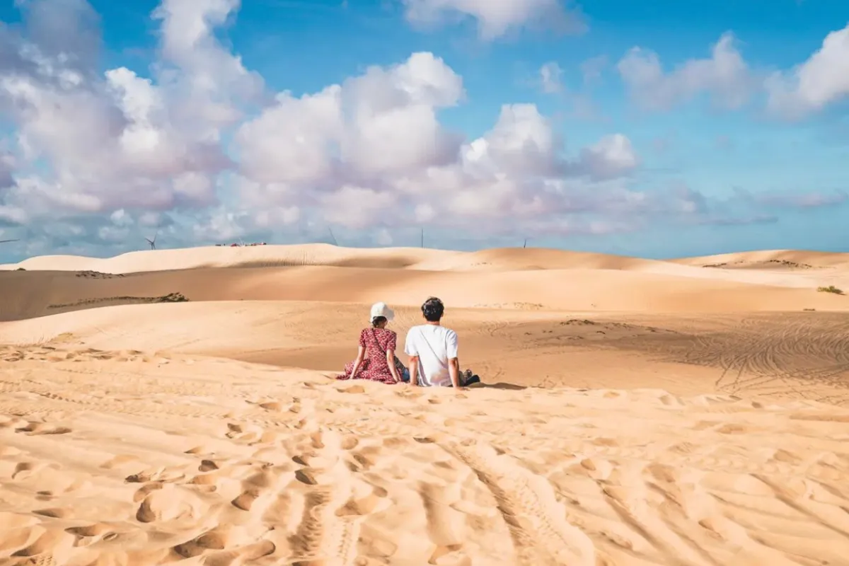 Couple sitting on the White Sand Dunes overlooking a tranquil lake near Mui Ne, Vietnam.