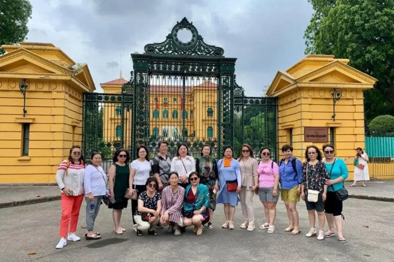 Group of tourists posing at the yellow Presidential Palace gate in Hanoi's Ho Chi Minh Complex