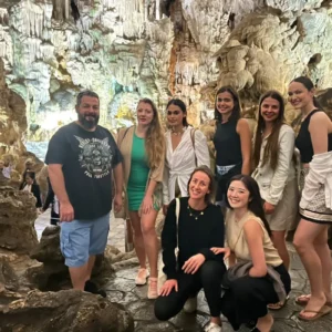 A group of travelers exploring illuminated stalactite formations inside a limestone cave in Halong Bay on their Vietnam package tour 7 days