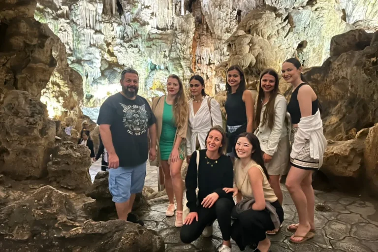 A group of travelers exploring illuminated stalactite formations inside a limestone cave in Halong Bay on their Vietnam package tour 7 days